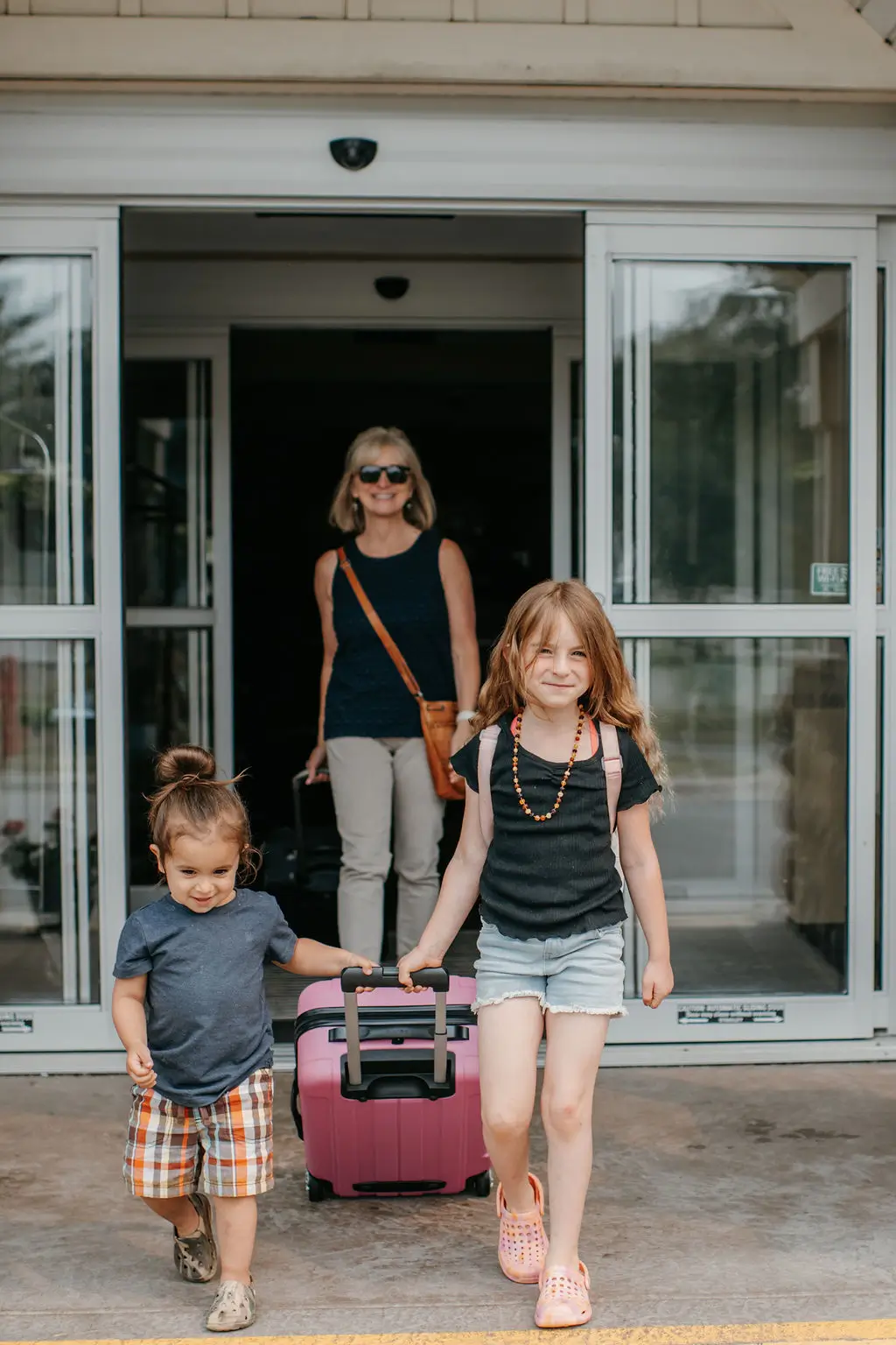 Woman and 2 kids walking out hotel door with luggage